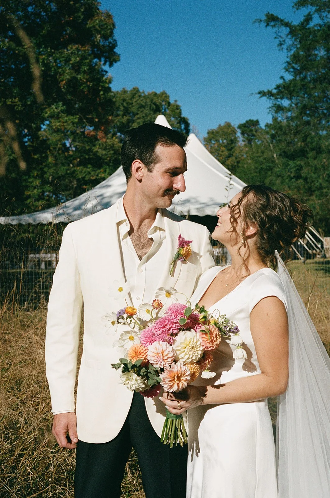 bride and groom smiling at each other with a tent in the background