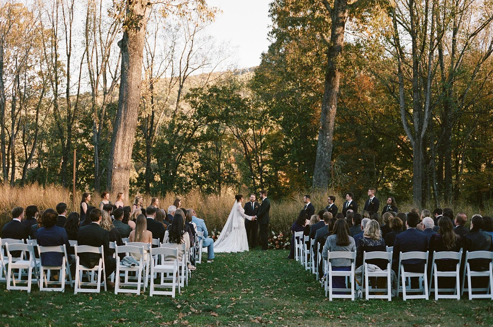 Outdoor wedding ceremony with bride and groom exchanging vows, surrounded by seated guests, in a wooded area during sunset. potters craft cider charlottesville va
