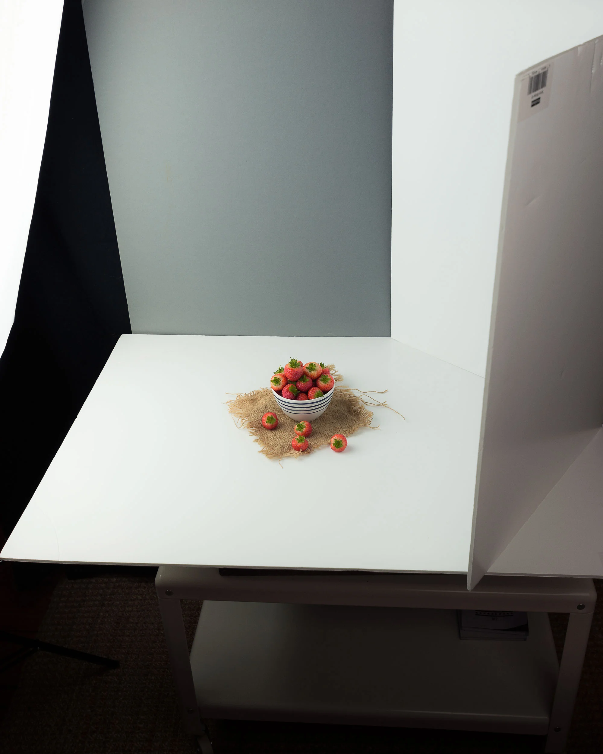 BTS of the strawberries shot above. I positioned a single soft box on the left hand side on 4/5ths power. The base card is semi gloss which reflects some of the light onto the underside of the strawberries and the bowl. On the right hand side I have a white semi gloss bounce card, folded to create two 45° angles. This bounces the light from the soft box back onto the front and back of the subject. I find this set up helps to create a more natural outdoor look with less shadow and contrast. The backboard is a soft grey bounce card, I edited this in post to have a bluer hue reminiscent of the sky. The small piece of hessian sack is used to create interest and I added a spoon to give the final image an anchor. I often find that the more simple the set up the stronger the final image is and this shot is definitely a good example of that philosophy. Soft Boxes