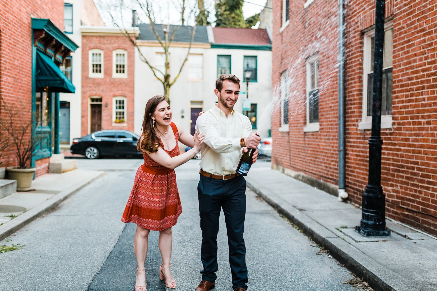 couple pops a champagne bottle during their engagement session in Baltimore