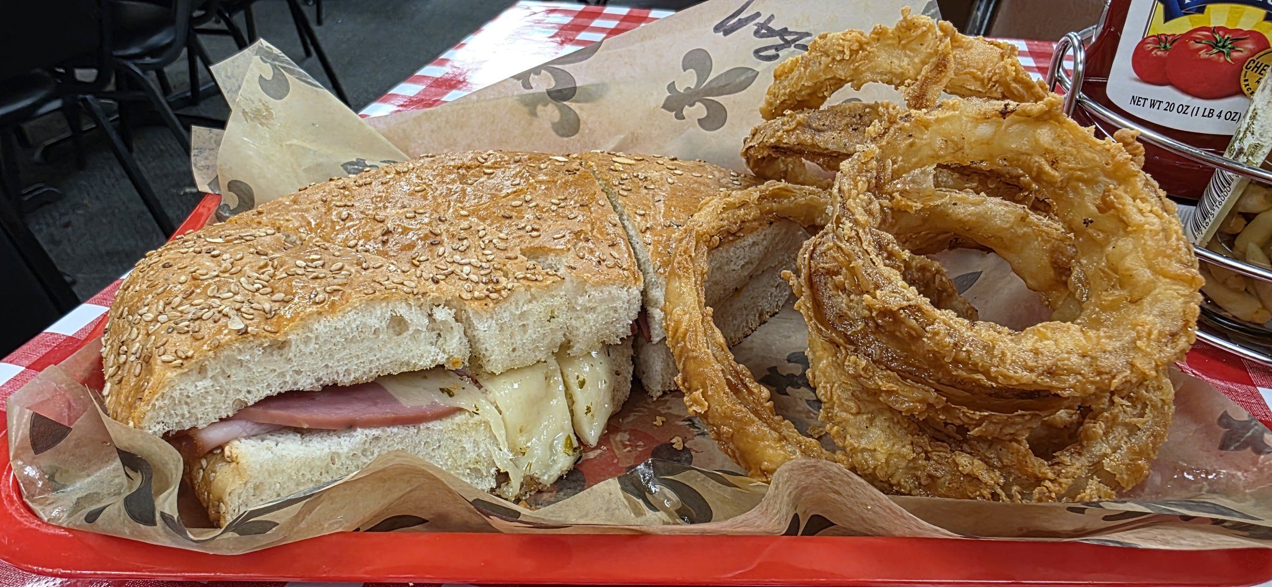 a traditional muffaletta sandwich served on a sesame seed bun and homemade onion rings