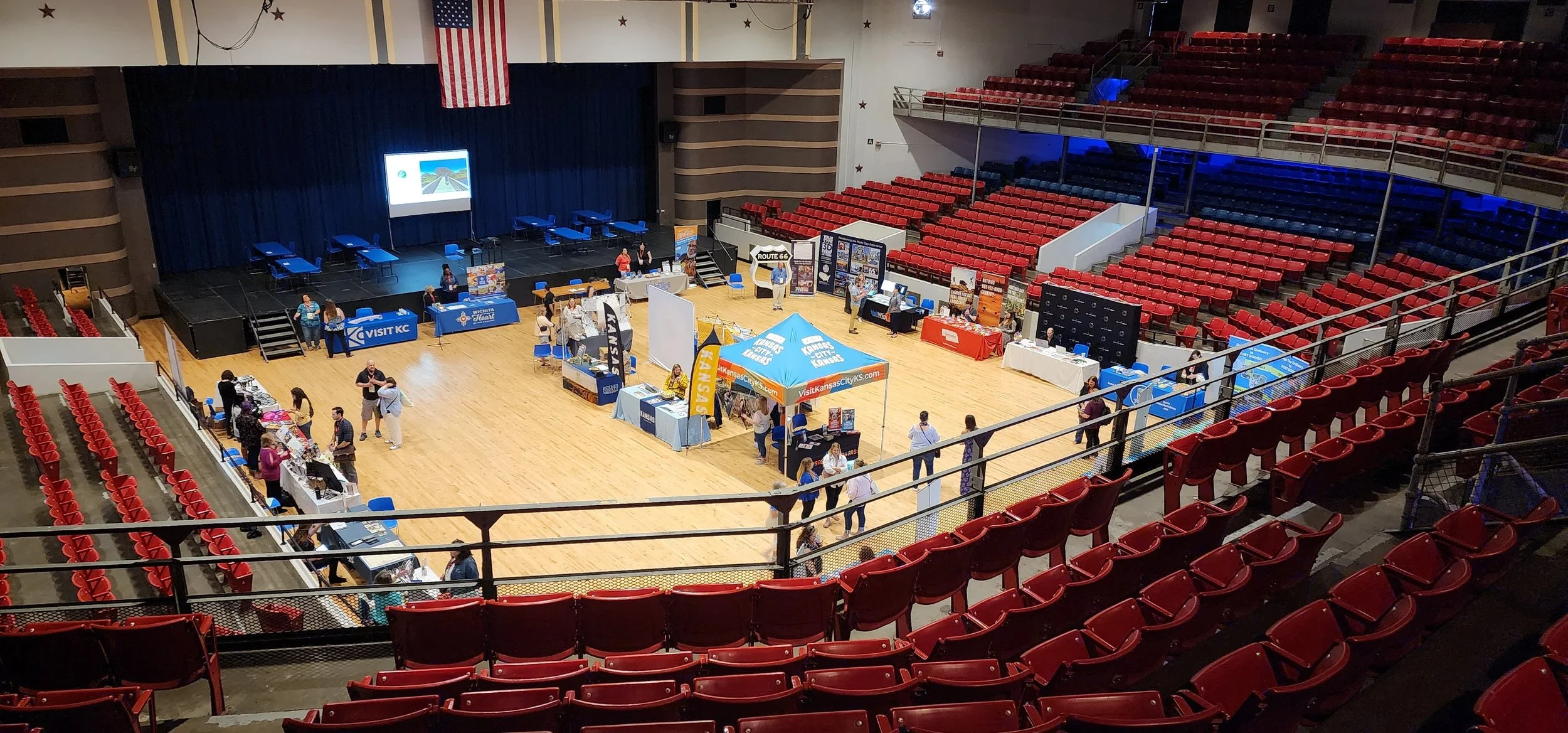 vendors set up on the floor of a 3000 seat arena. Stage is in the background and the seats are red