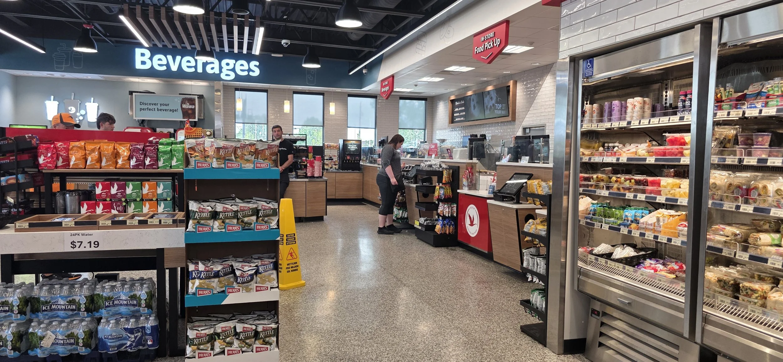 a glowing sign spelling out beverages hangs high on the wall inside a WaWa. It is located near the counter where you order food.