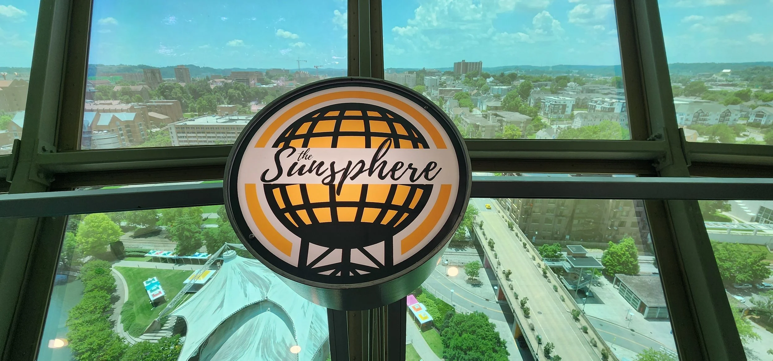 A circular sign with the words the Sunsphere on it. Windows above and below it reveal a city skyline and mountains
