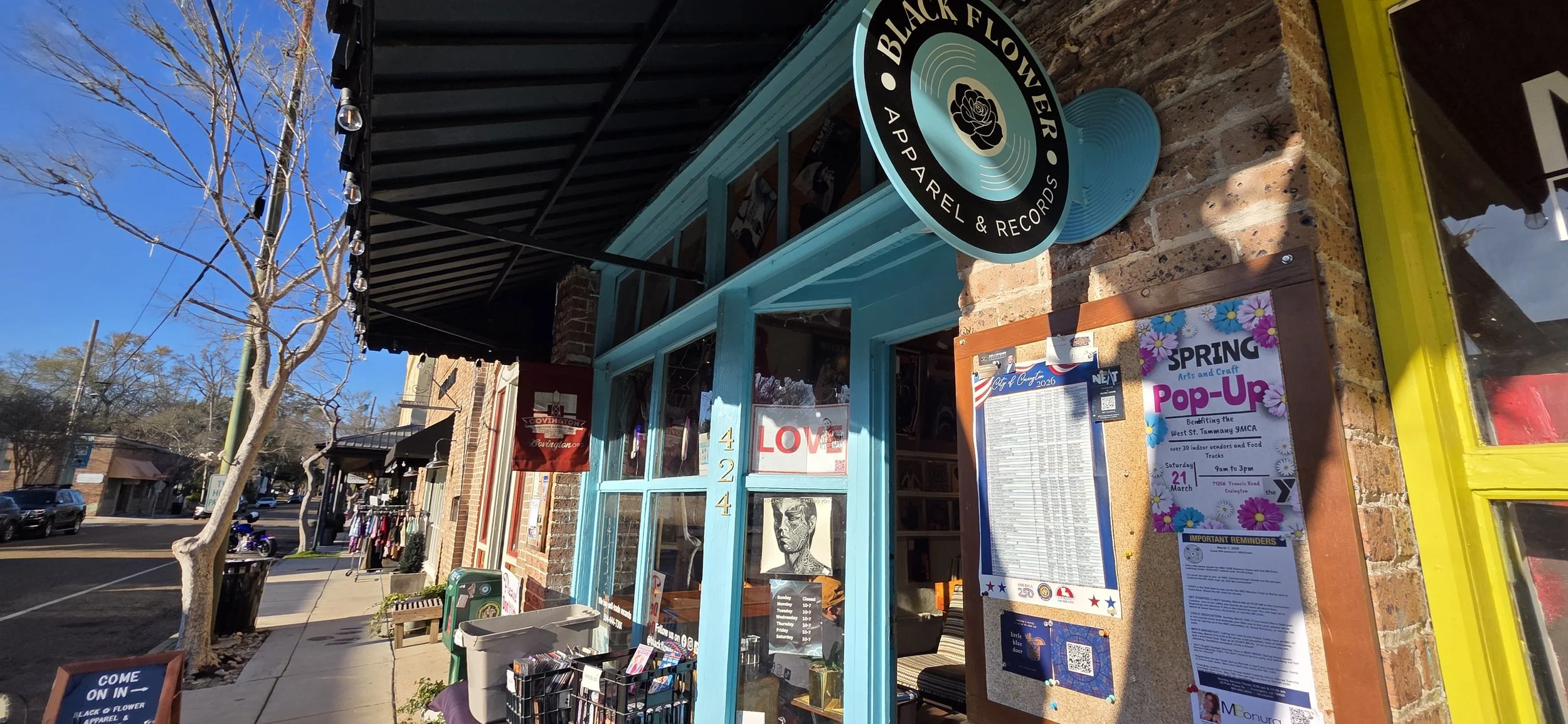 Brick building with a large windowfront painted a turquoise like color. A small record shaped sign with the lwords Black Flower Apparel and Records sits to the right of the door.
