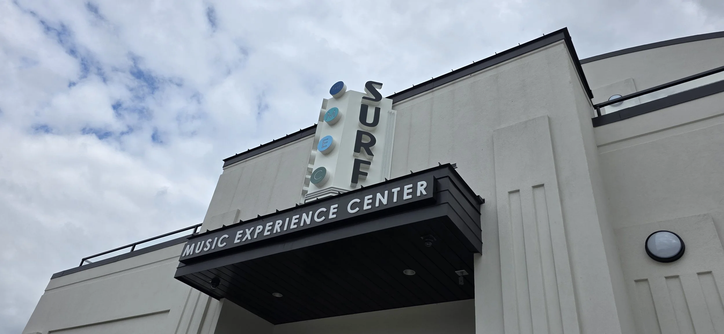 Entrance to a white building with  the words Surf Music Experience Center