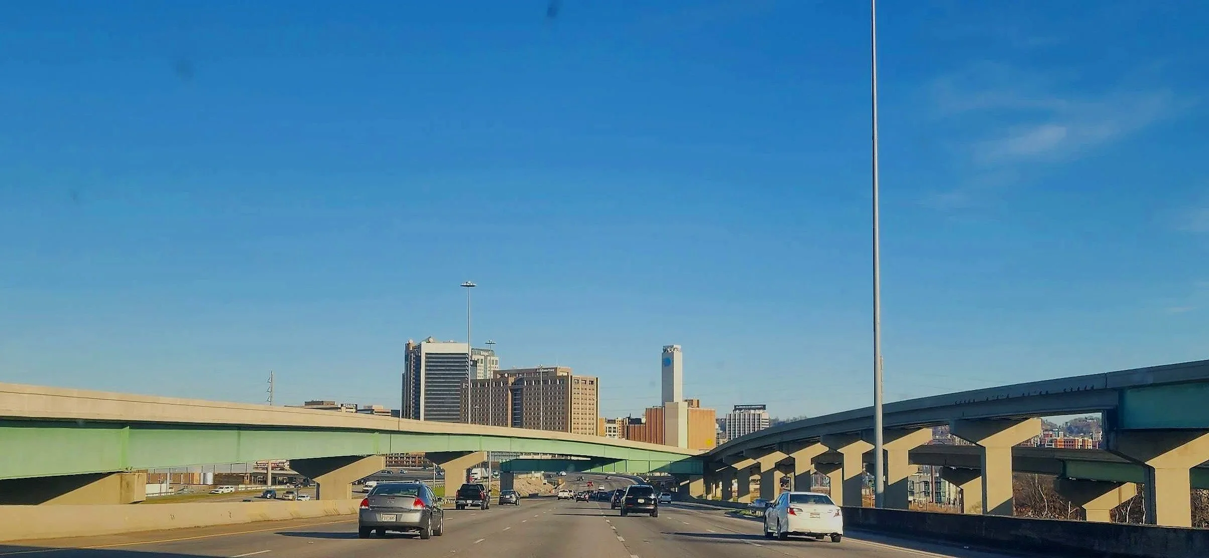 5 lanes of interstate traffic moving toward overpasses. Tall buildings in the distance make up downtown Birmingham Alabama