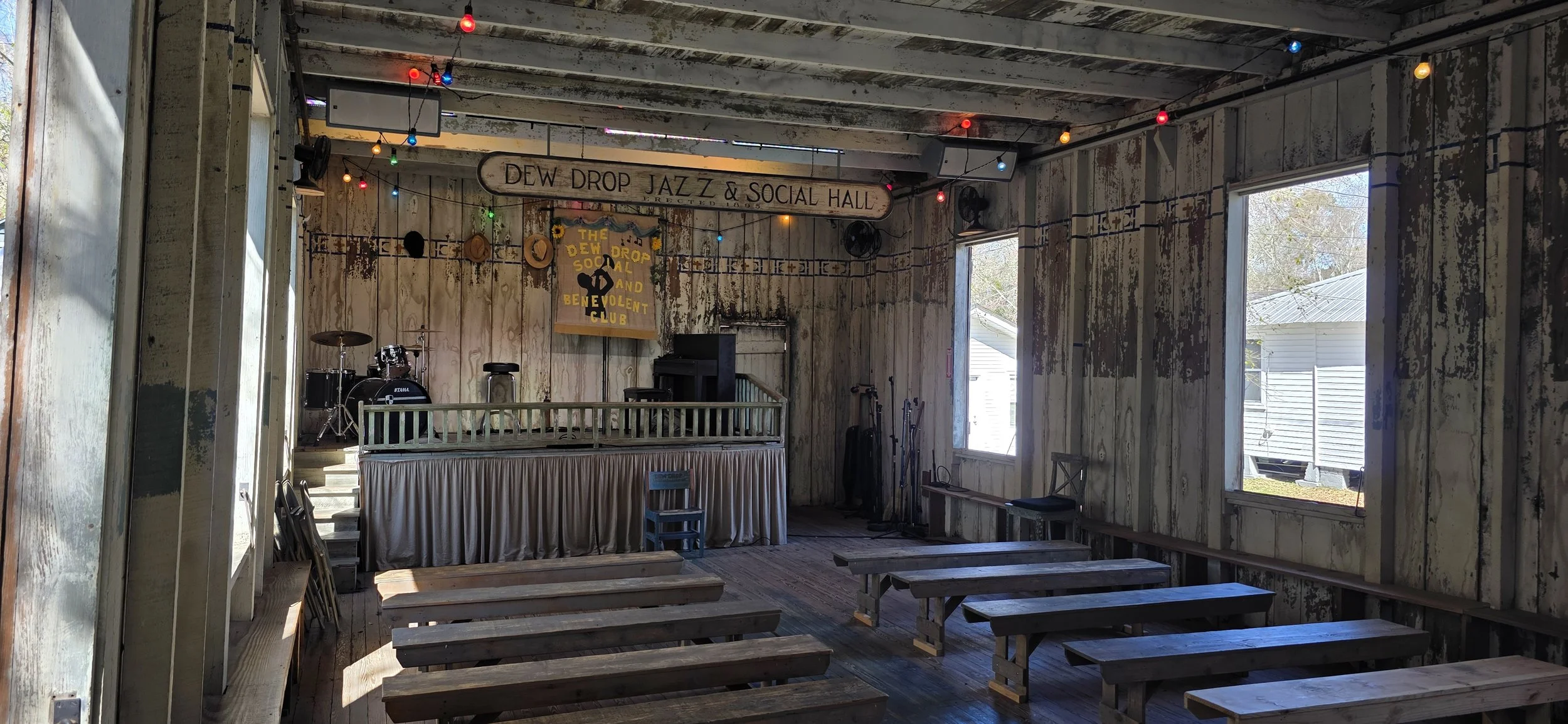 an old wooden building with large windows.  a small stage is in the back with a sign saying dew drop jazz and social hall