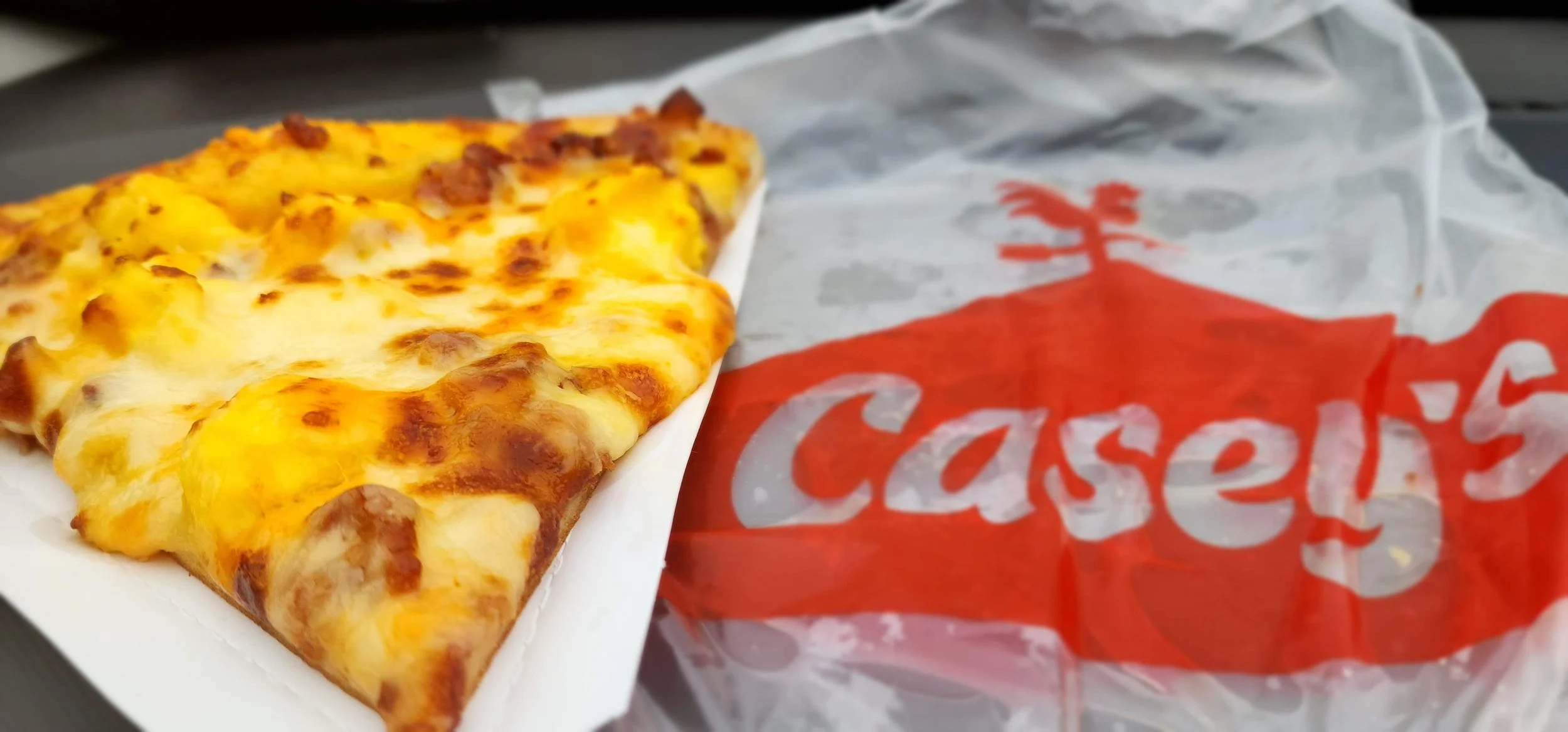 slice of breakfast pizza next to a plastic bag with the Casey's logo