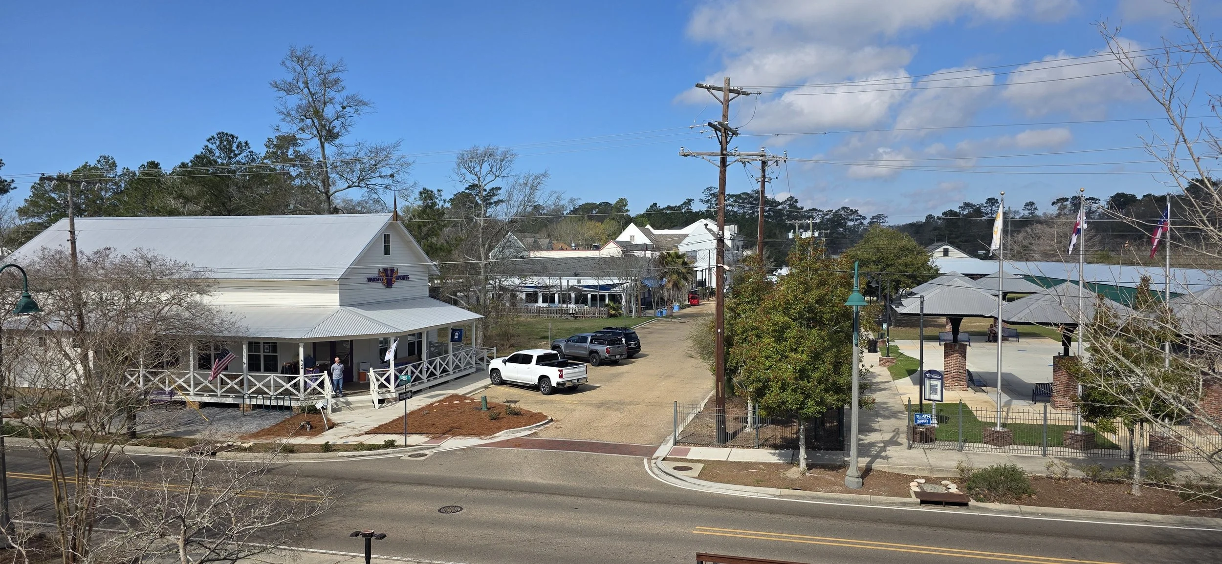 A few small buildings line up along a small street with a park off to the right in Mandeville Louisiana with a park