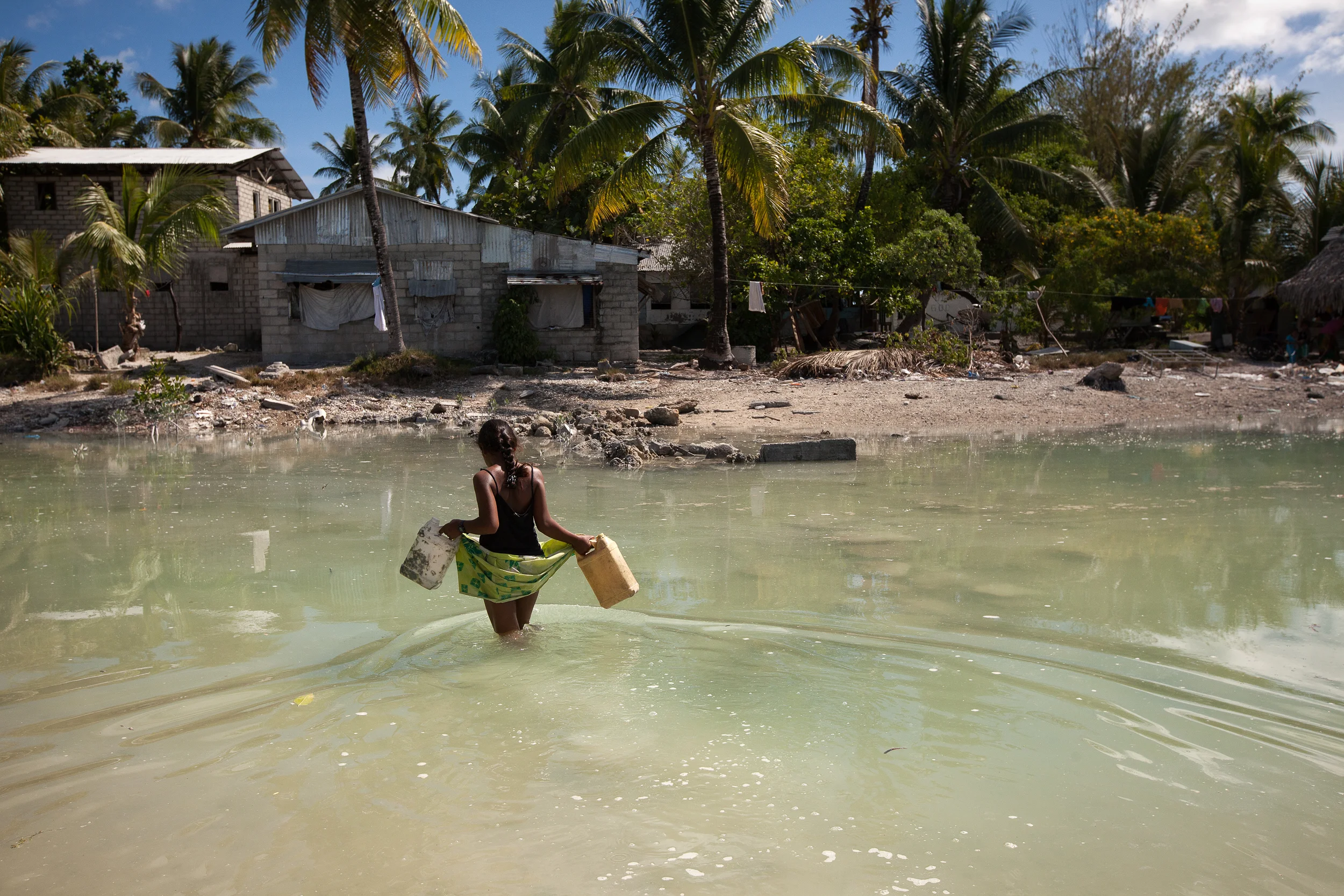 A young girl crosses the lagoon at high tide to get some water for her family who live on a thin strip of sand that gets cut off from the main island every high tide.