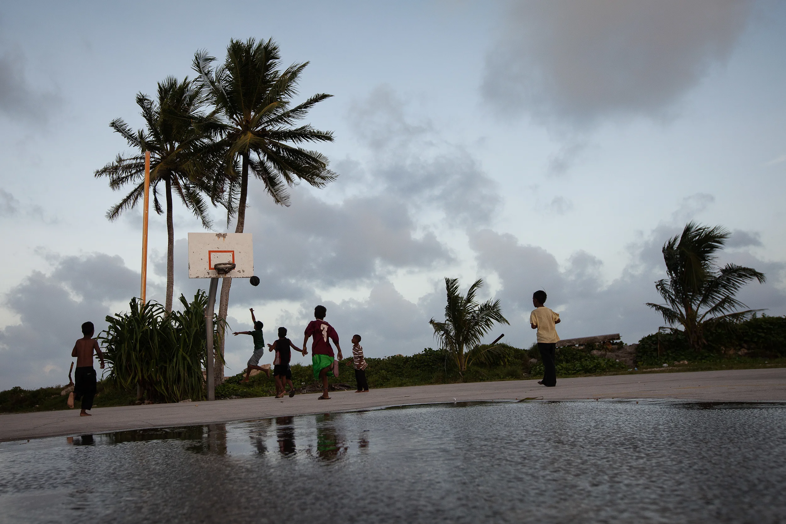Young boys play basketball in Majuro after a storm. Basketball is the most popular sport in the Marshall Islands, and many children want to grow up and play in the United States. Marshallese are free to live and work in the US under a Compact of Free Association, making that the most likely destination should they have to leave their islands.