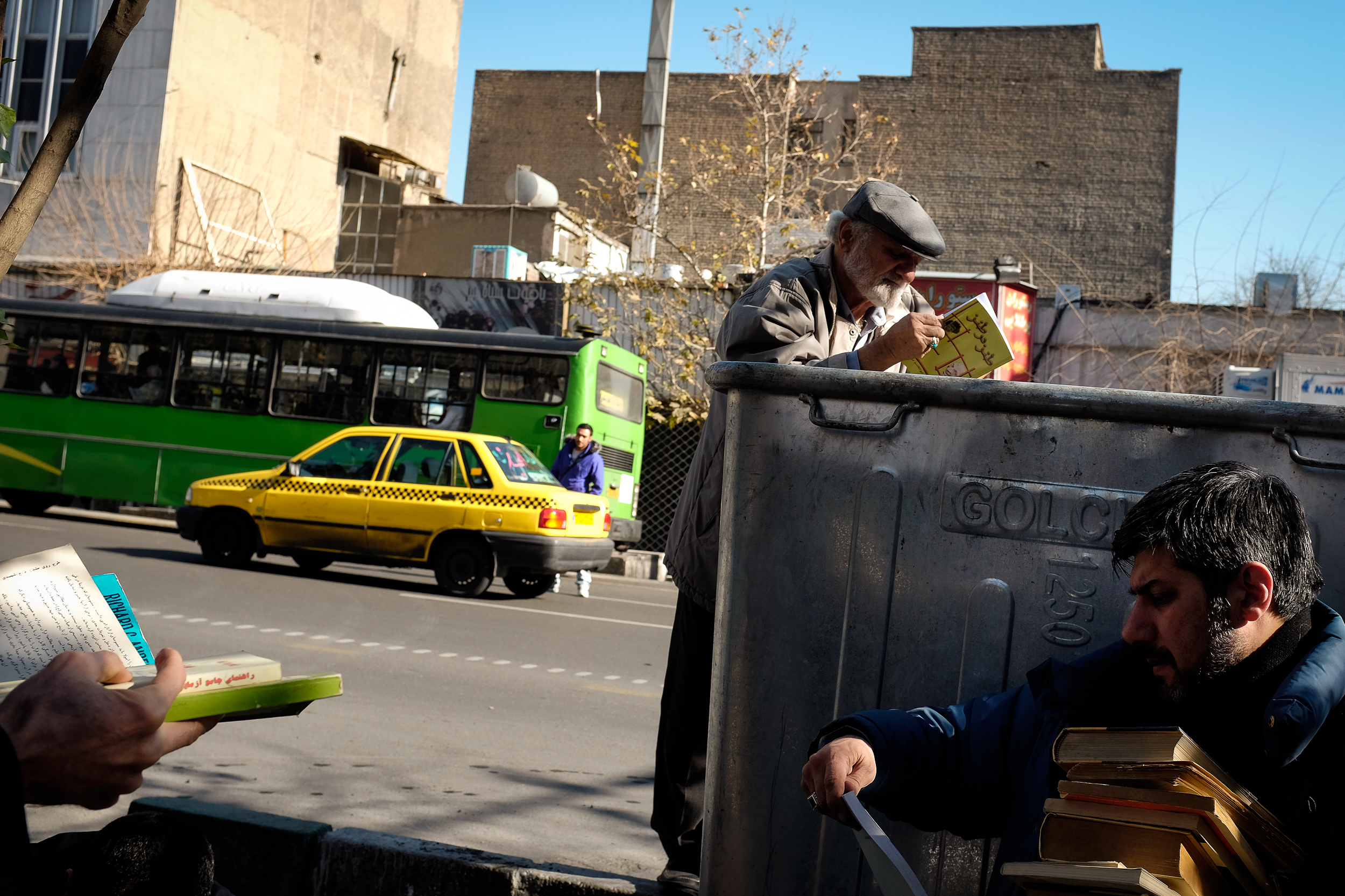 Men skim through a pile of discarded books on the side of a road in central Tehran.