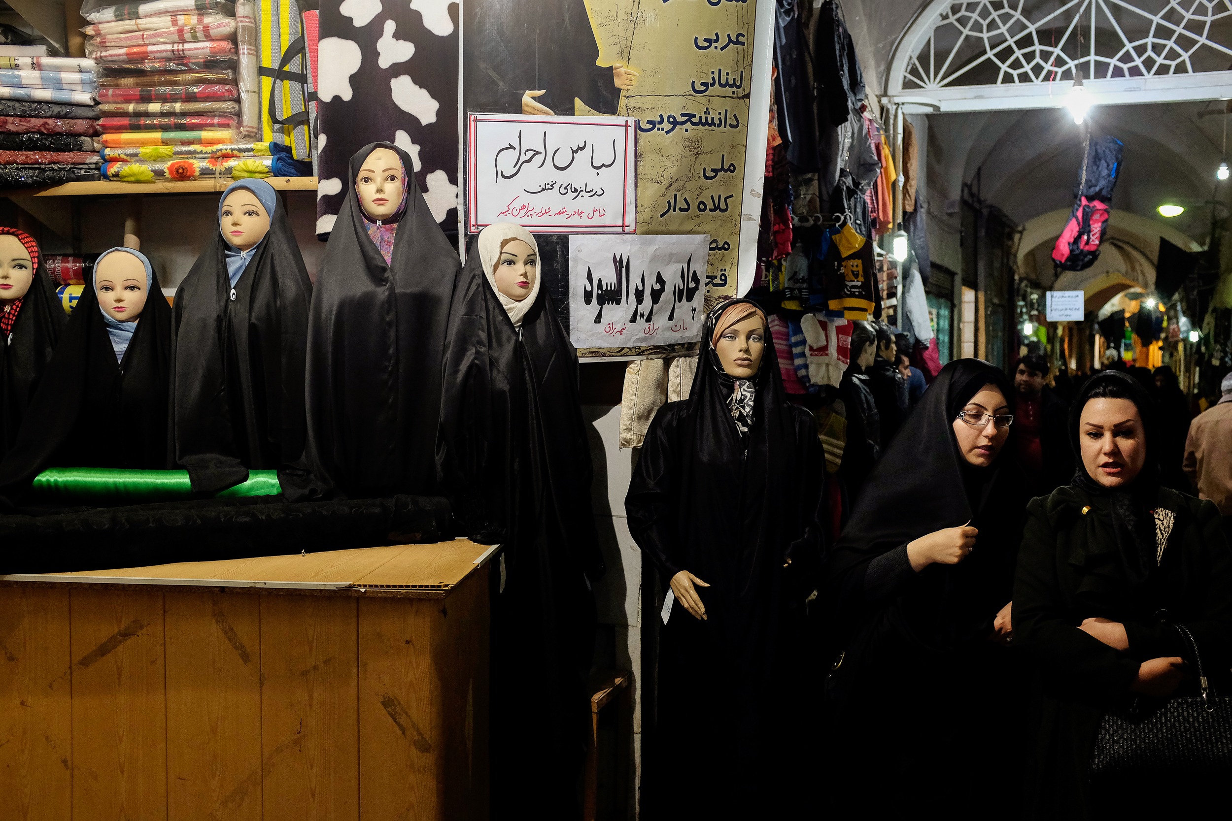 Two women walk past a store selling cloth in Kashan.