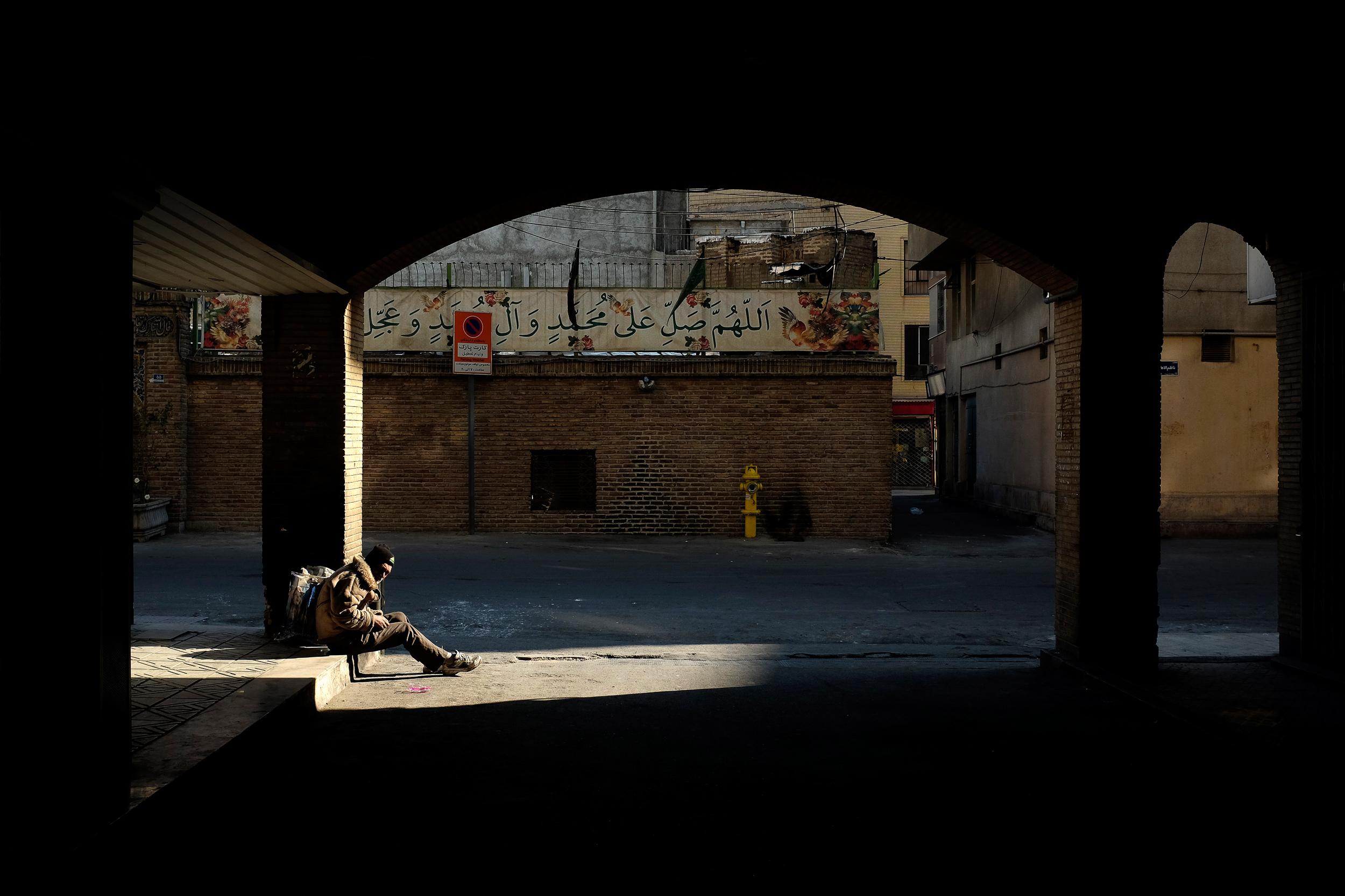 An addict is illuminated by the sun under a bridge in Central Tehran.