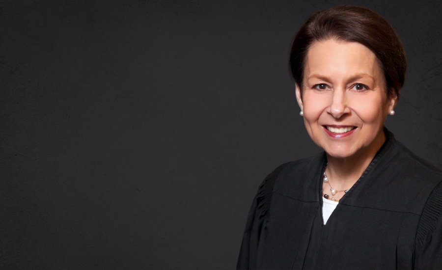 U.S. District Judge Nancy G. Edmunds, smiling, in a black judicial robe and pearl earrings against a dark gray background.