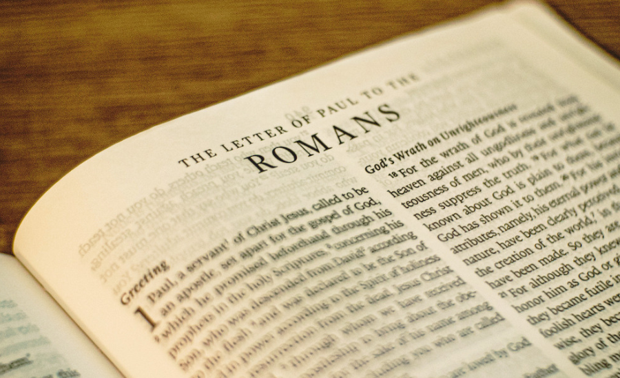 Open Bible turned to the Letter of Paul to the Romans, resting on a wooden surface