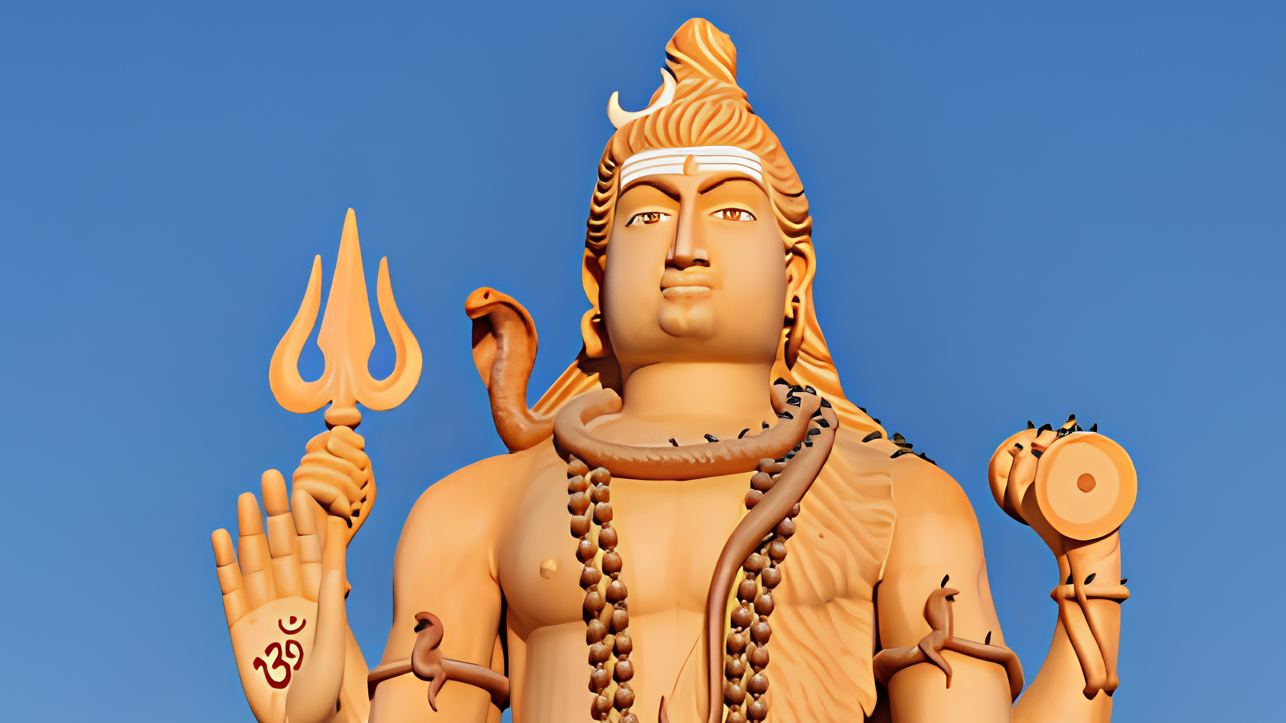 A large orange statue of the Hindu deity Shiva holding a trident and a small drum, with snakes coiled around its neck and arms and an Om symbol on its raised palm, set against a blue sky.