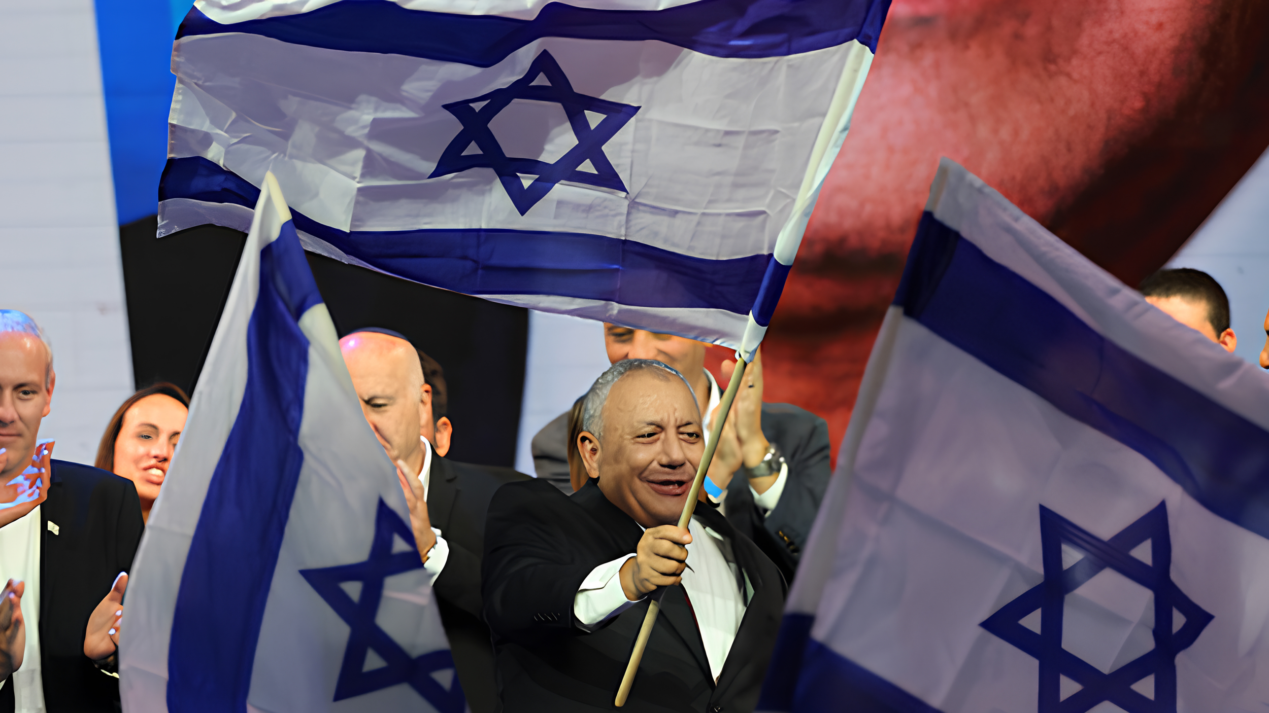 Gadi Eisenkot smiles and waves an Israeli flag on stage at his party’s election-night rally in Tel Aviv, surrounded by applauding supporters and more waving flags.