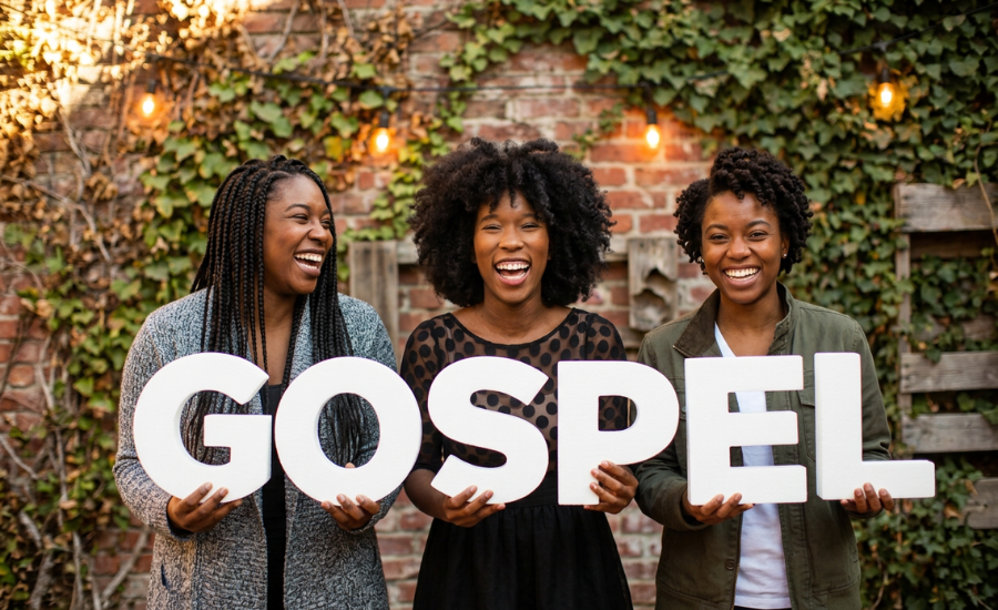 hree joyful women holding large letters spelling the word GOSPEL in front of an ivy-covered brick wall