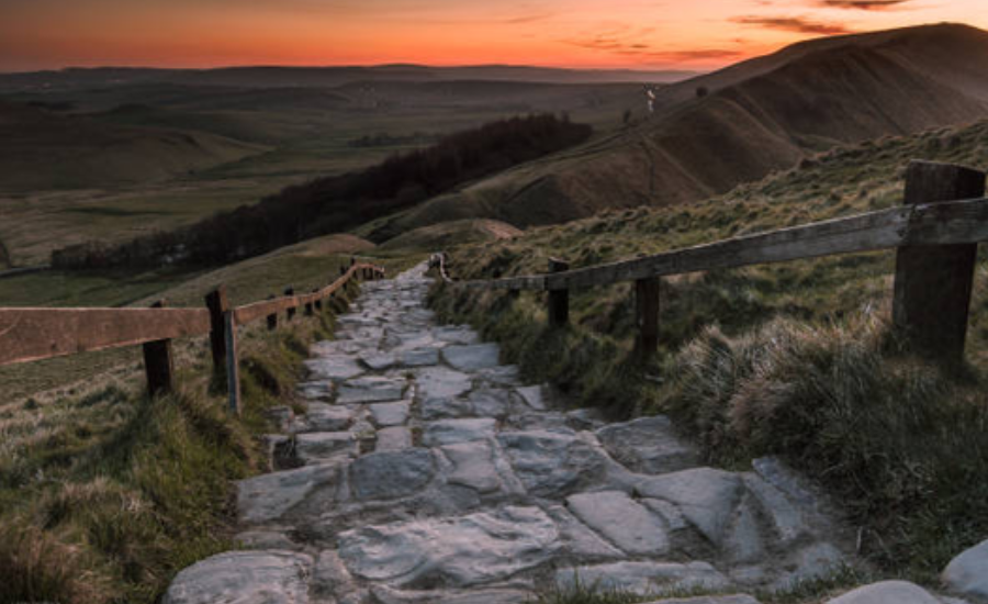 Stone pathway winding through hills at sunset, framed by wooden fencing