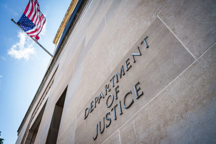 The exterior of the U.S. Department of Justice building in Washington, D.C., with the department's name engraved in stone and an American flag overhead