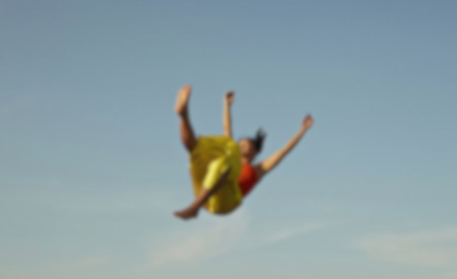A person wearing a yellow dress and red top falling through an open blue sky, photographed with motion blur.