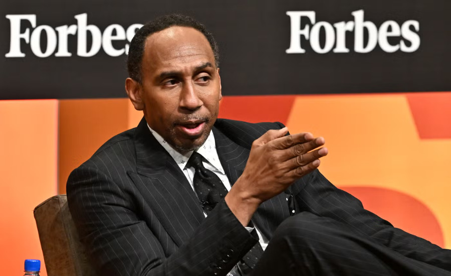 Stephen A. Smith speaks onstage at the 2025 ForbesBLK Summit, seated in a dark pinstripe suit and gesturing with one hand in front of a Forbes backdrop.