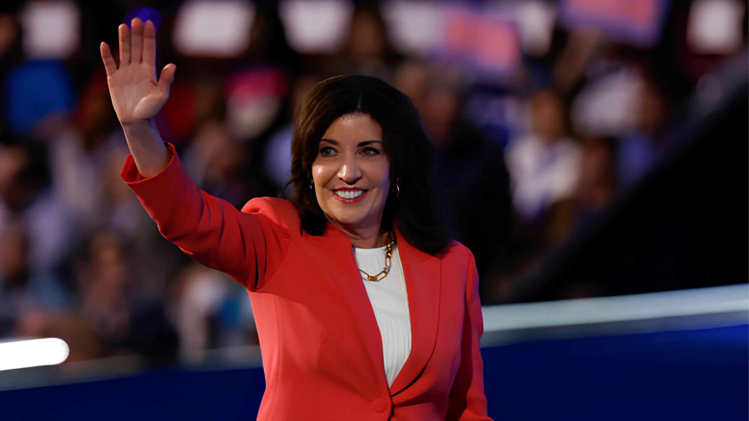 New York Gov. Kathy Hochul, wearing a red blazer, smiles and waves to a crowd at the 2024 Democratic National Convention.