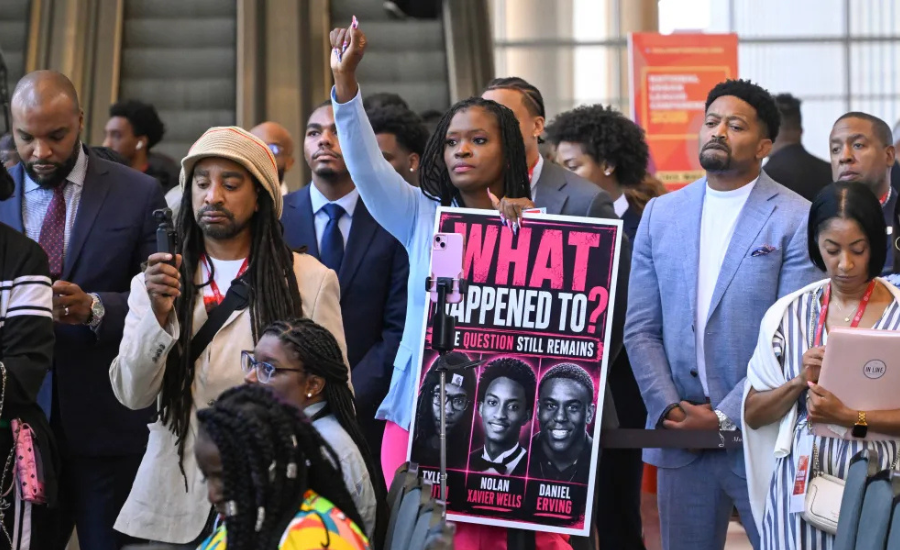 Celina Charles raises her hand while holding a sign asking what happened to Nolan Wells and Daniel Erving during a news conference at the National Urban League’s annual conference in Nashville, Tennessee.