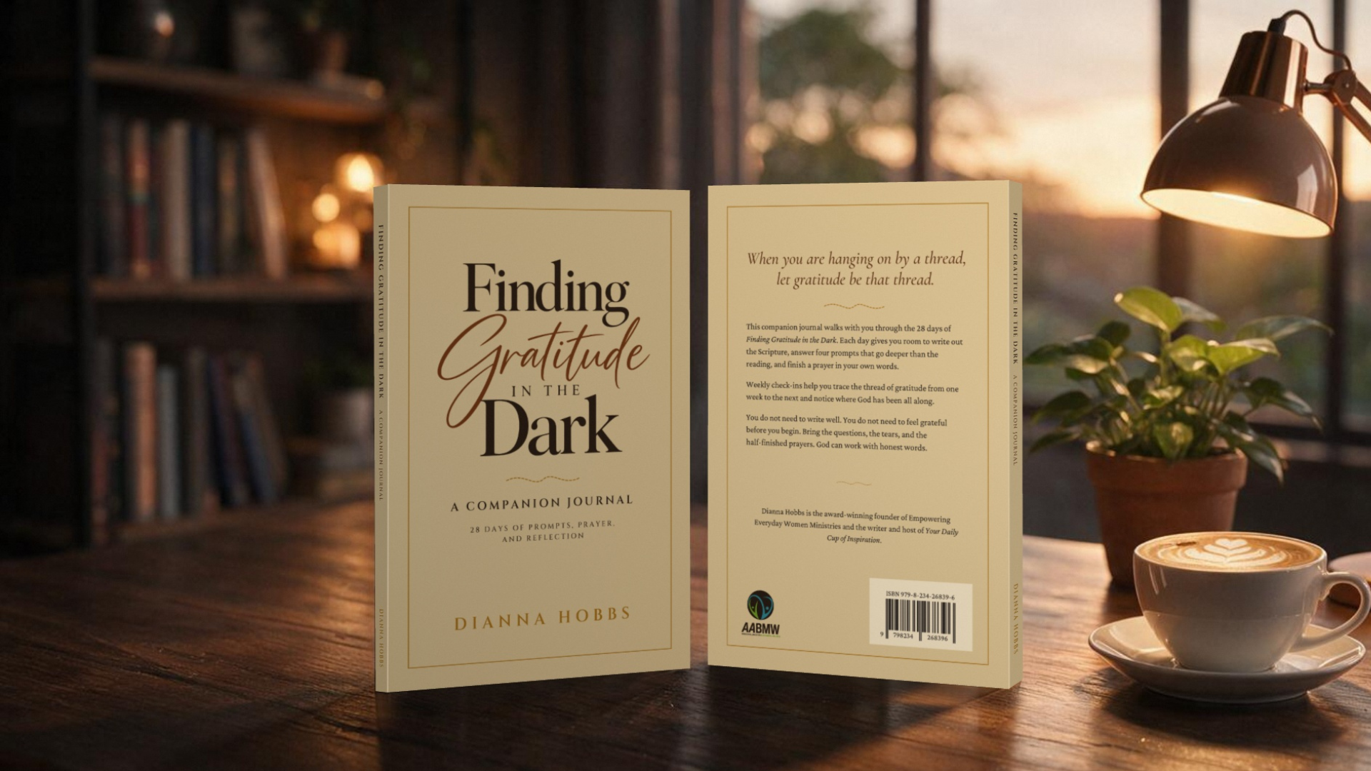 Front and back covers of Finding Gratitude in the Dark: A Companion Journal by Dianna Hobbs standing on a wooden desk beside a desk lamp, a potted plant and a latte.