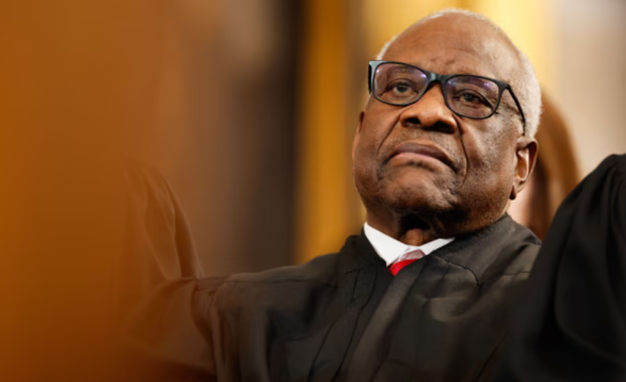 Supreme Court Justice Clarence Thomas wearing glasses and a black judicial robe, gesturing during a public appearance.