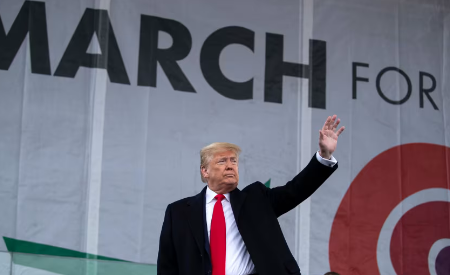 President Donald Trump waving from a stage in front of a large March for Life banner in Washington D.C.