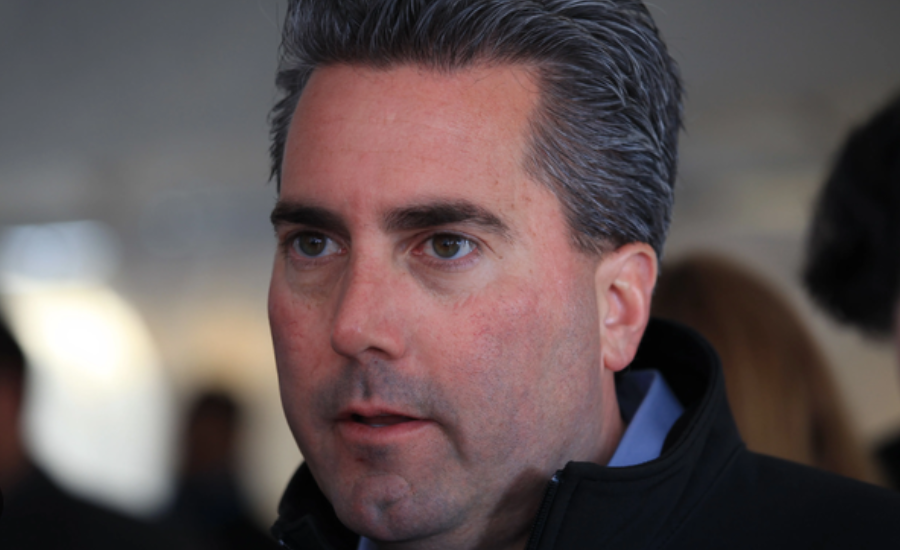 Kevin Adell, with slicked-back graying hair, wearing a dark jacket over a blue collared shirt in a crowded indoor setting.