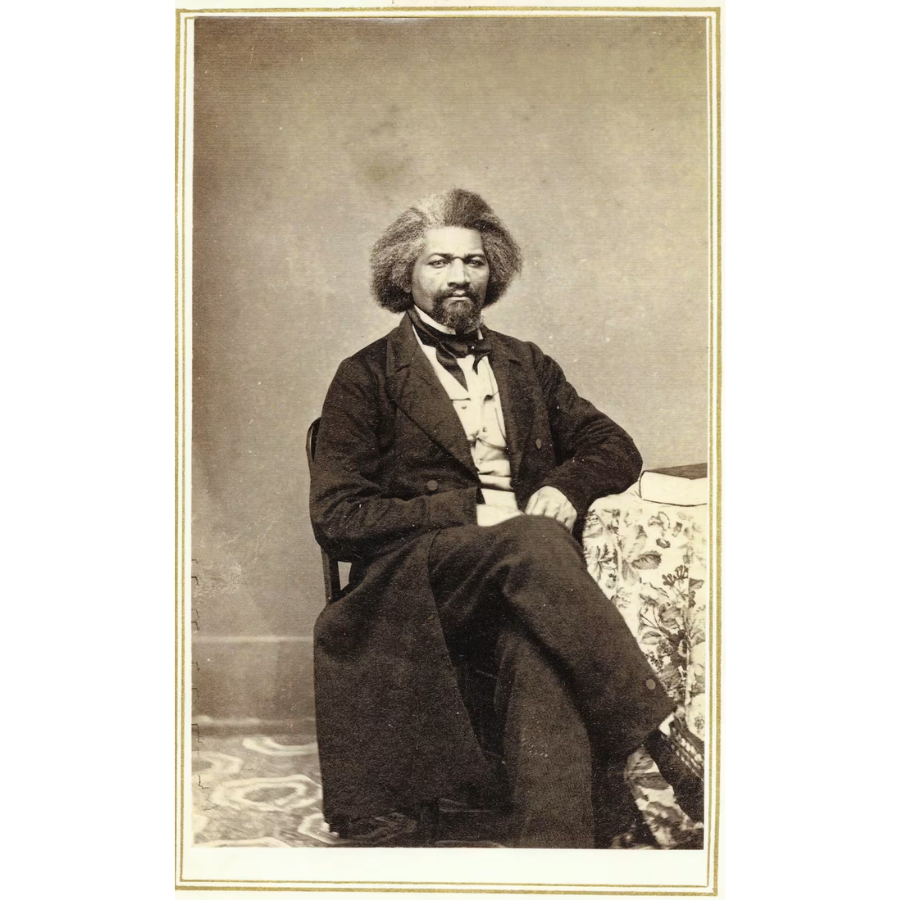 A sepia-toned carte de visite photograph of Frederick Douglass seated in a chair, wearing a dark formal coat and vest with a white shirt, taken at Hillsdale College on January 21, 1863.