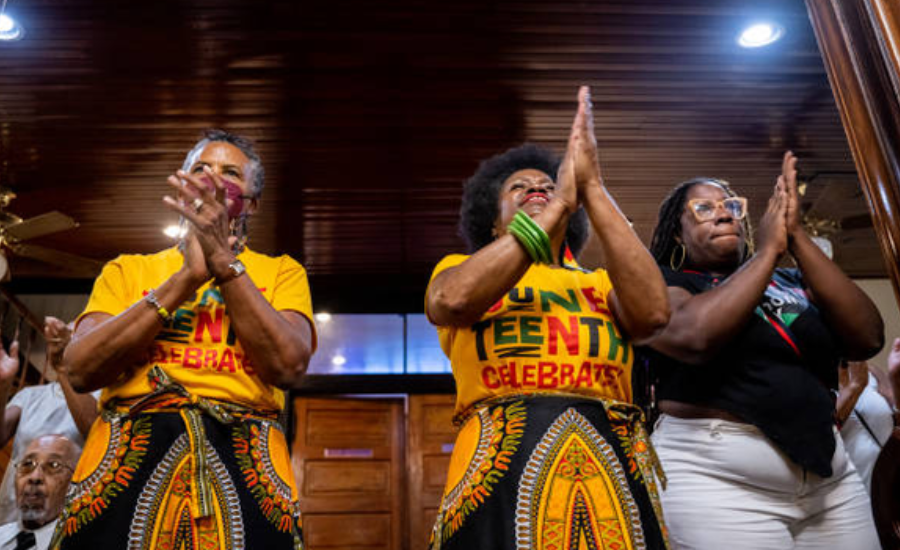 Three Black women in yellow Juneteenth Celebrates T-shirts and African-print skirts clap their hands during a church service inside Reedy Chapel A.M.E. Church in Galveston, Texas.