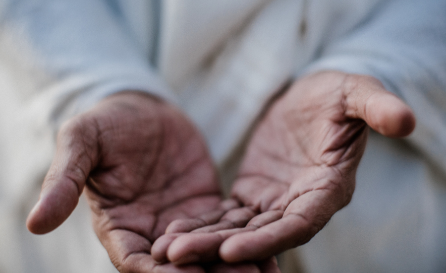 Close-up of a person’s weathered hands held out together, palms up, against light-colored clothing.