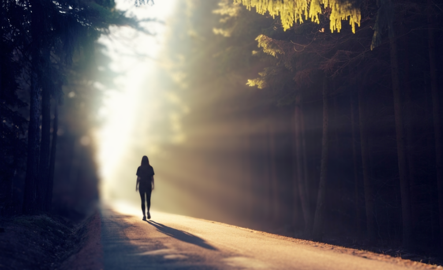A woman walking a wooded path toward bright light breaking through the trees, illustrating the journey from idolatry's grip toward the unshakable foundation of Christ