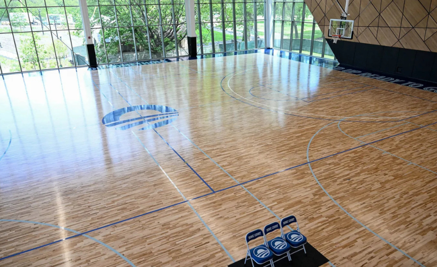 An indoor basketball court with polished hardwood floors and floor-to-ceiling windows inside the Home Court building at the Obama Presidential Center
