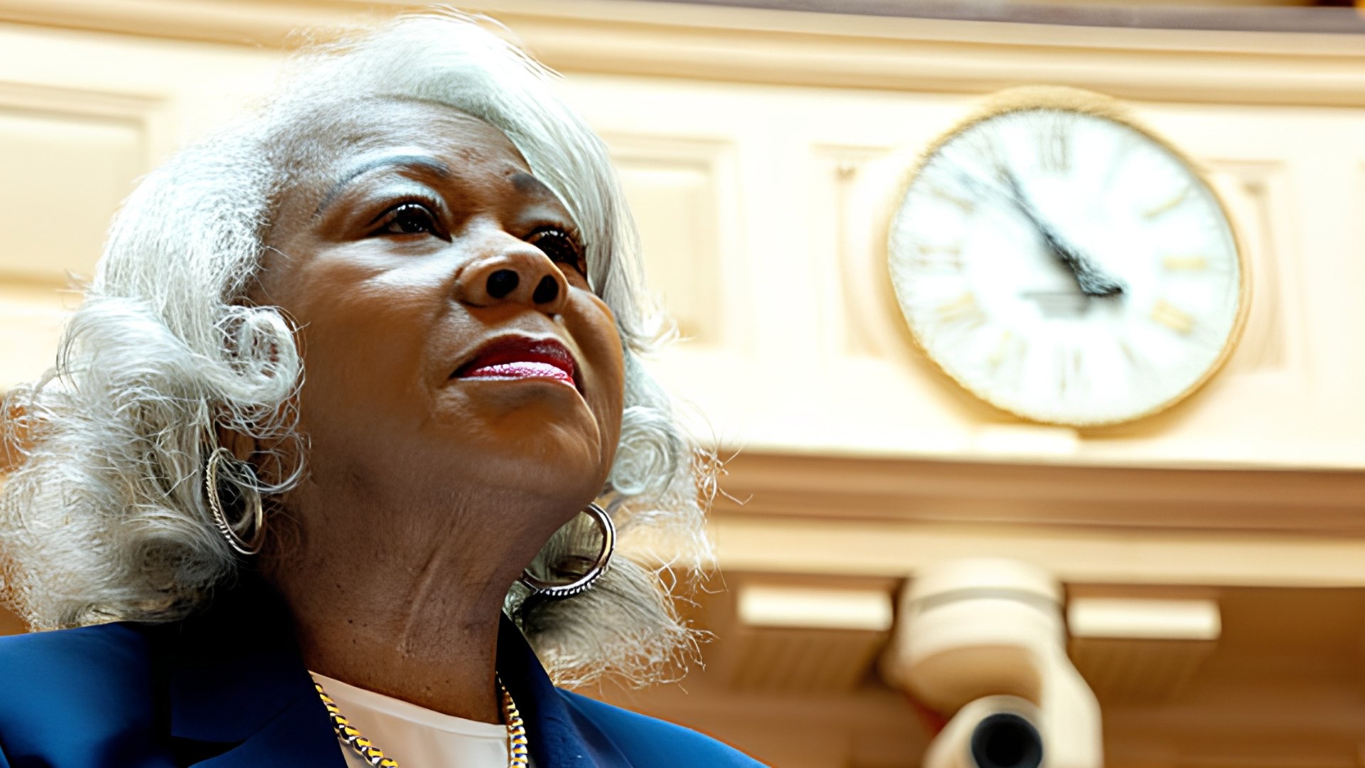 L. Louise Lucas, wearing a navy jacket and hoop earrings, looks upward in the Virginia Senate chamber with a large clock on the wall behind her.