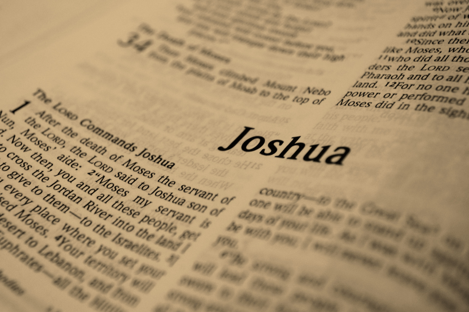 Close-up of an open Bible turned to the beginning of the Book of Joshua, with the word “Joshua” in sharp focus on warm sepia-toned pages.