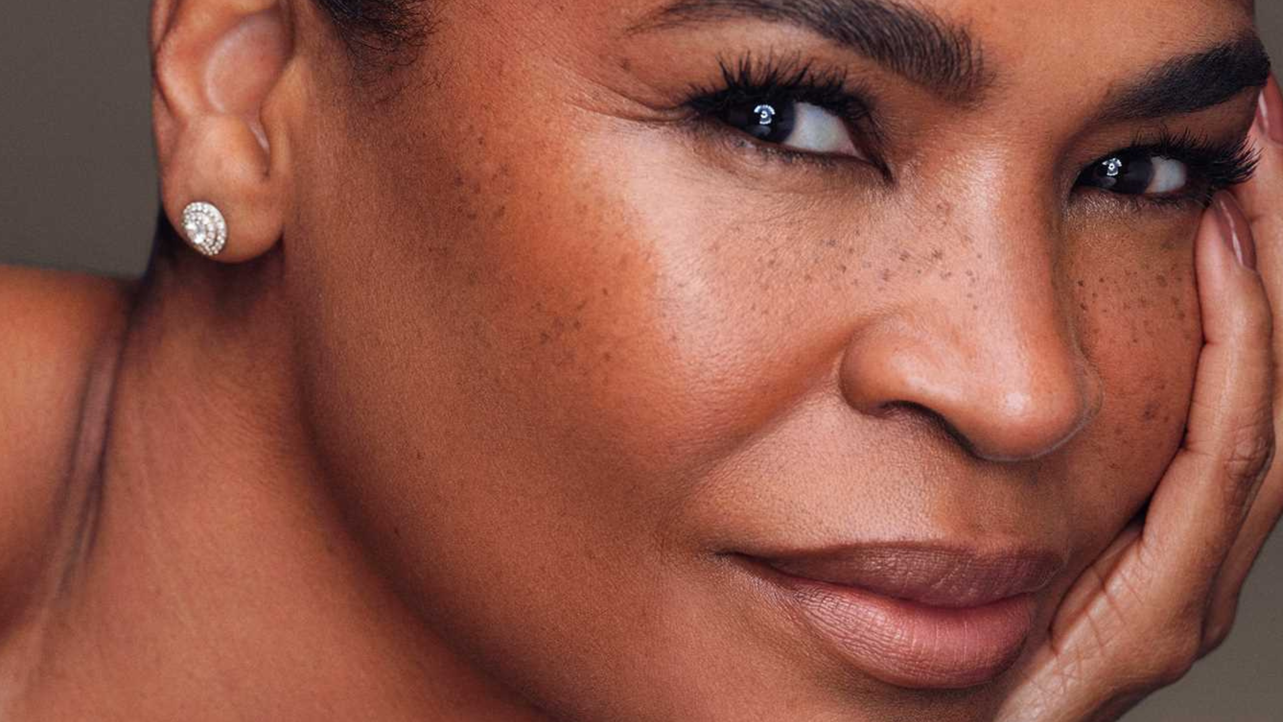 Close-up of Nia Long resting her cheek on her hand, freckles across her face and a diamond stud in her ear, in the warm-toned portrait from her memoir’s cover.
