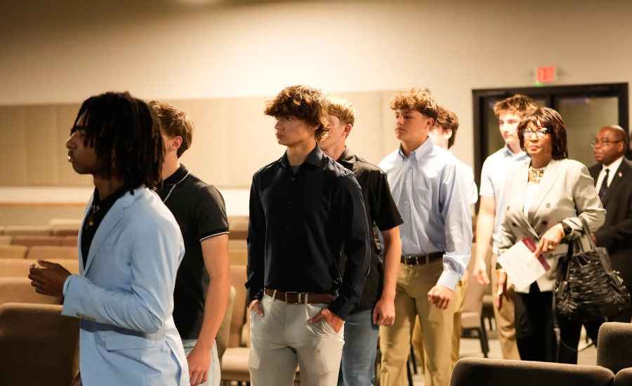 A line of young men, including football teammates, filing into a memorial service, followed by an older woman and man