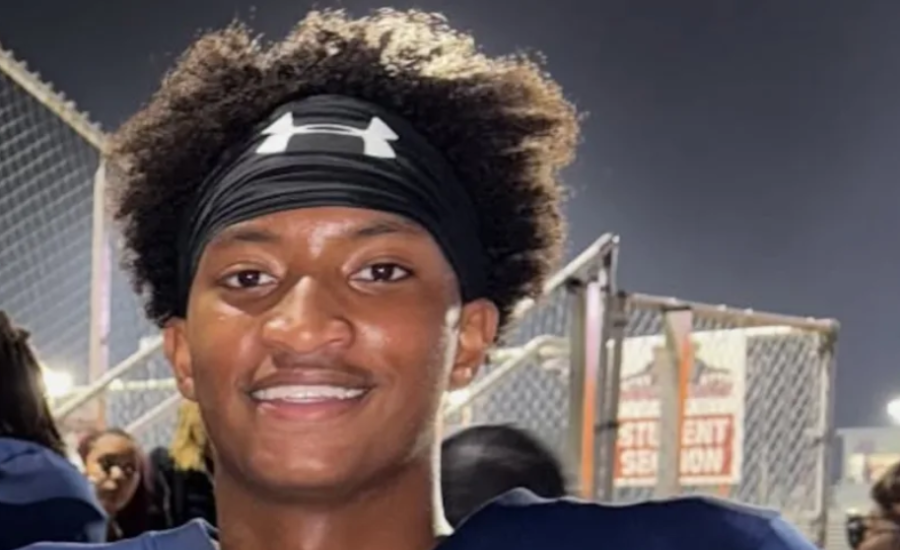 Nolan Wells, an 18-year-old wearing a black Under Armour headband and navy jersey, smiling at a football game