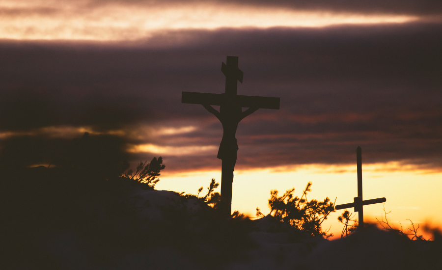 Silhouette of the cross of Christ against a glowing sunset sky at Calvary
