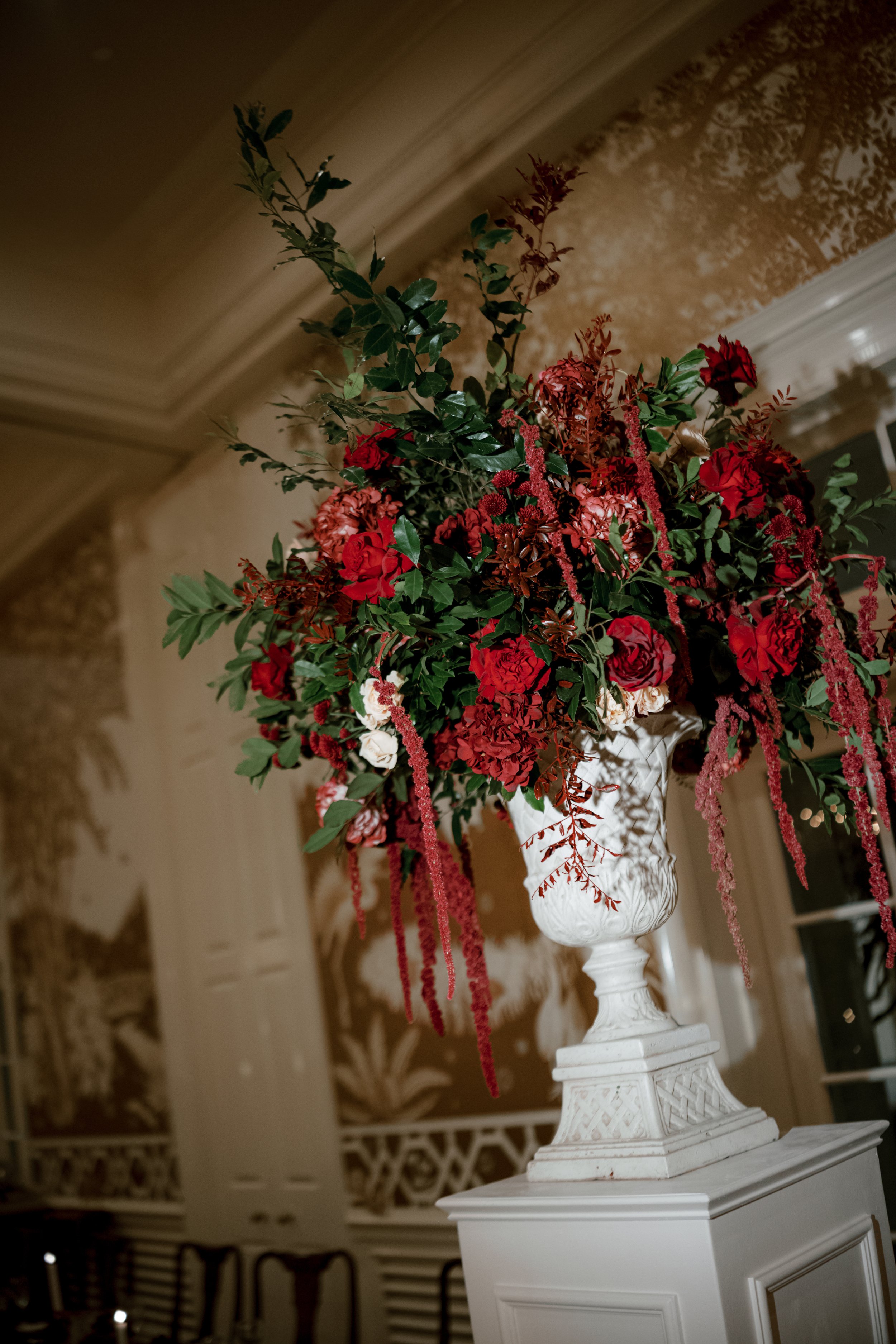 Grand floral urn installation at the Junior League of Houston. Deep red roses, cascading amaranthus, and wild greenery spilling from a classic white urn.