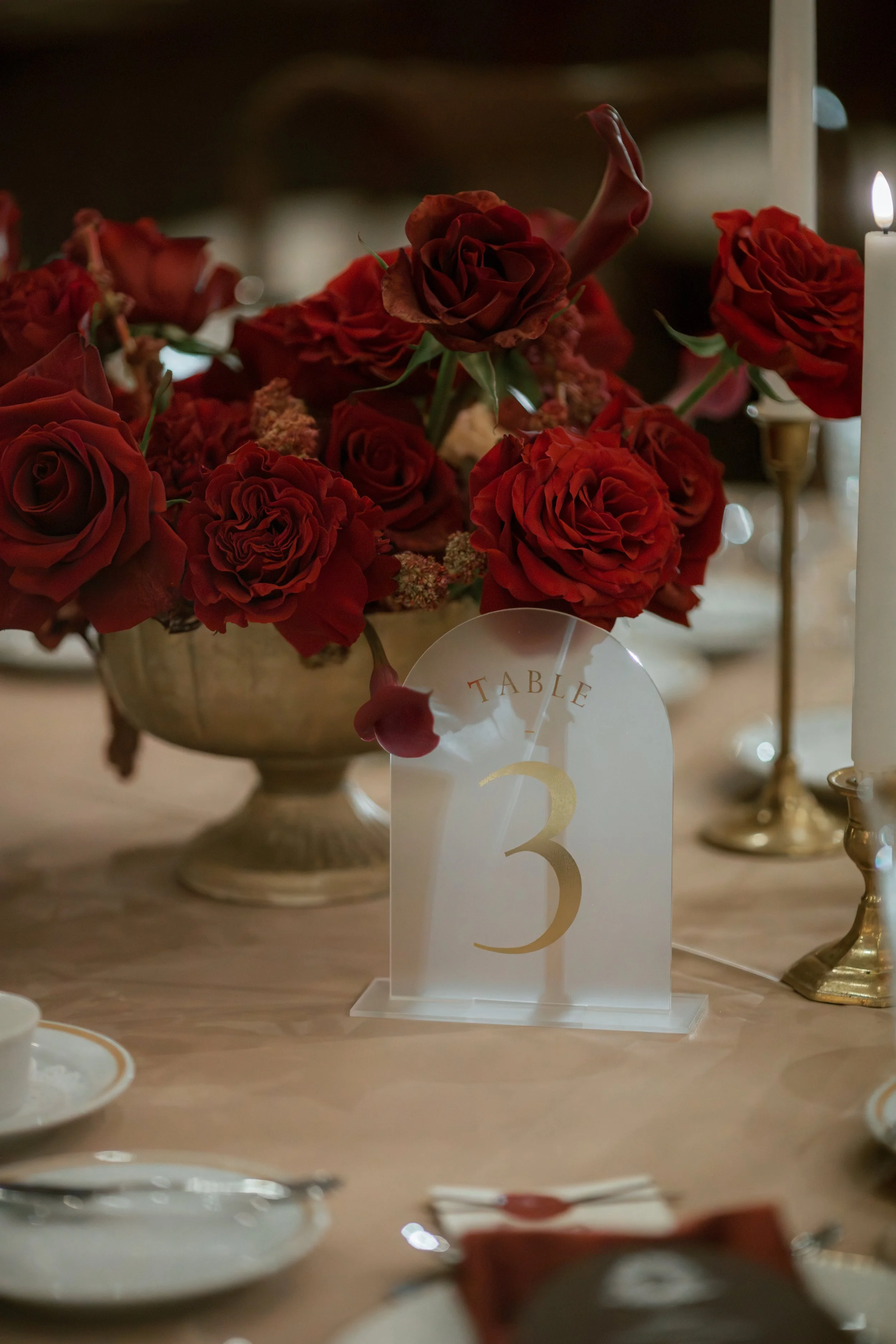 Lush red rose low centerpiece in gold bowl with gold candlesticks at Junior League of Houston wedding reception.