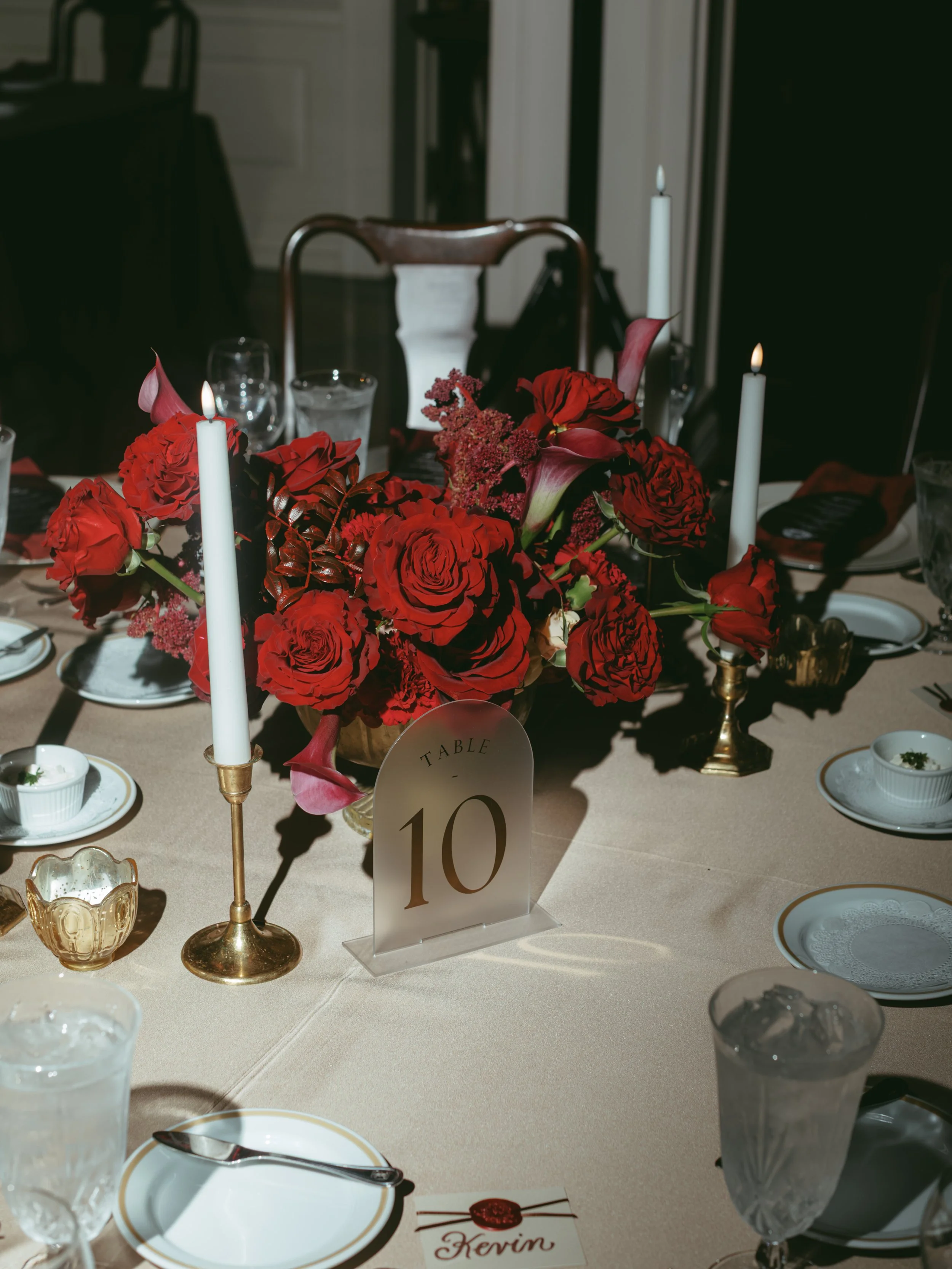 Lush red rose low centerpiece in gold bowl with gold candlesticks at Junior League of Houston wedding reception.