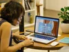 A woman with short brown hair and glasses using a laptop at a wooden table, browsing the Seleni Institute online training website.
