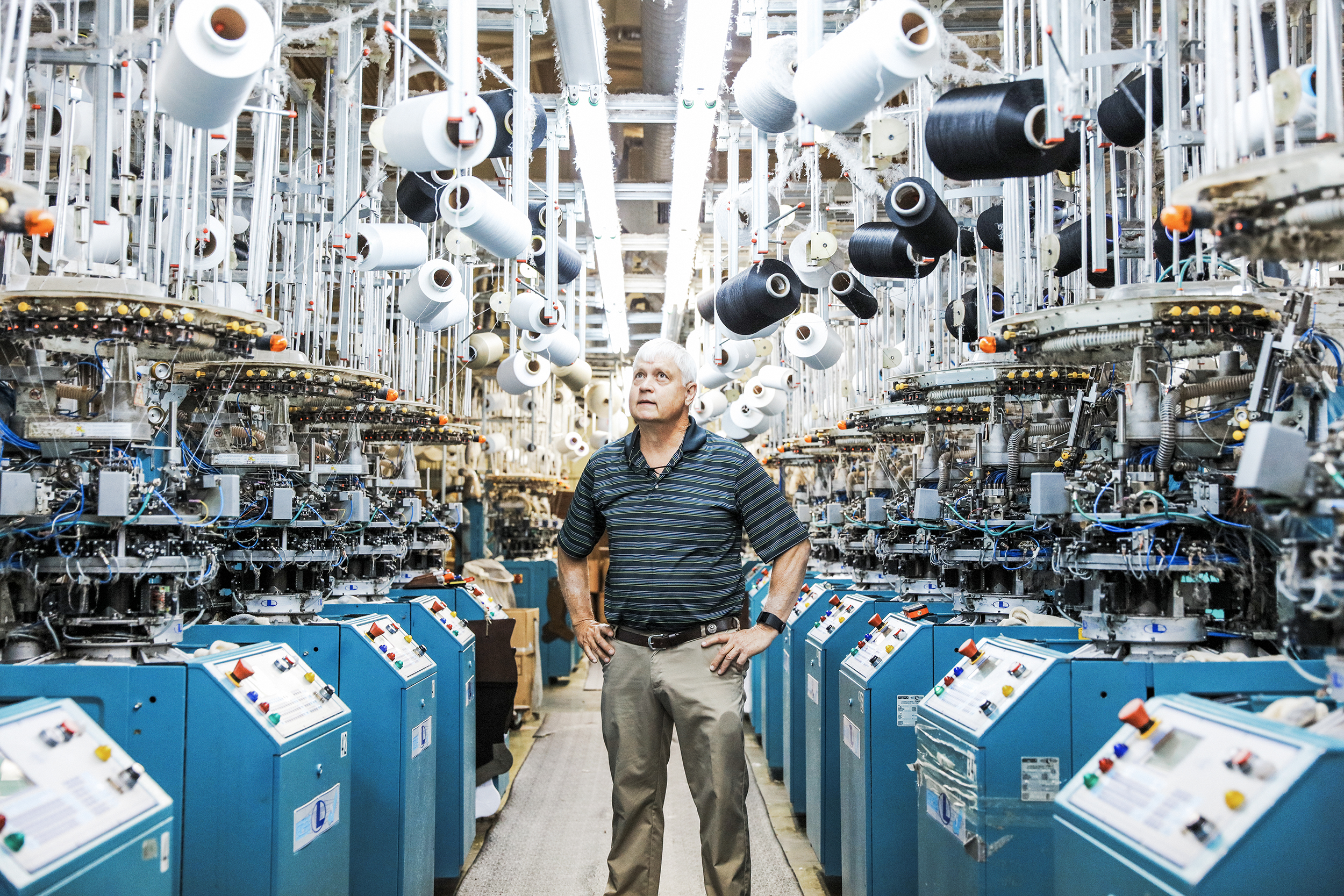 A man standing in between sock making machines. 